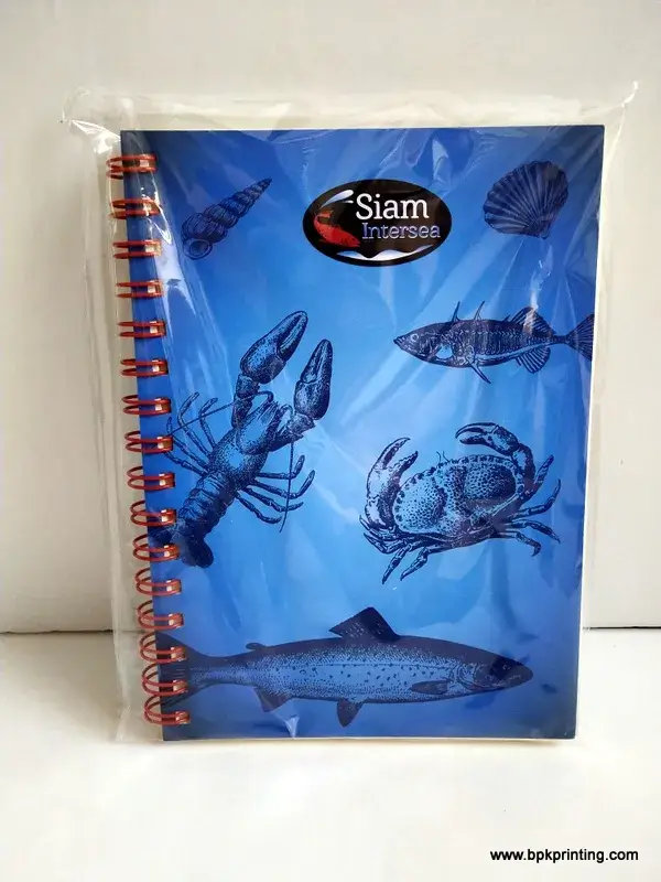 สมุดโน้ตพรีเมียมปกแข็งพิมพ์โลโก้ Siam Intersea พื้นหลังสีน้ำเงินพร้อมภาพวาดอาหารทะเล เช่น ปู ปลา กุ้ง เข้าเล่มแบบสันห่วงสีแดง บรรจุในถุงพลาสติกใส ผลิตโดยโรงพิมพ์ BPK Printing รองรับงานพิมพ์สำหรับธุรกิจอาหารทะเลและโลจิสติกส์ครบวงจร